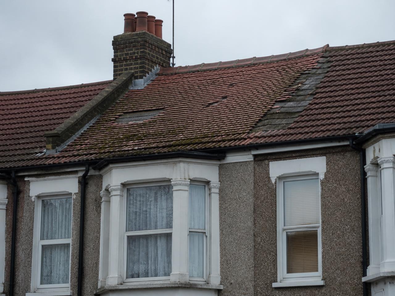 Worn roof with slipped tiles and moss before replacement