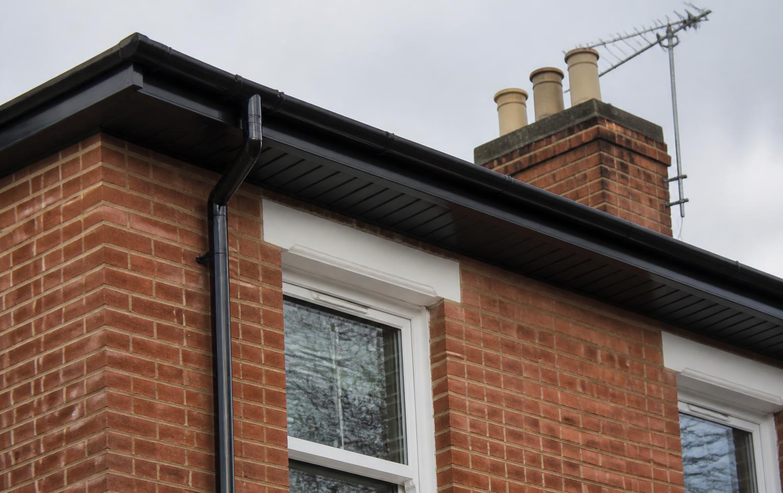 Newly fitted black guttering, fascia and soffit on a brick property